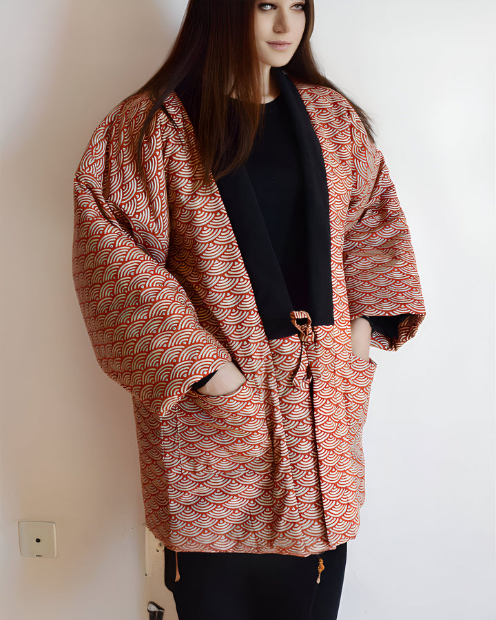 Femme portant un kimono rouge et beige à motif d'ondes, avec une bordure noire. Kimono ample avec poches, noué à la taille. Vêtements de style japonais, vente de kimonos en ligne.