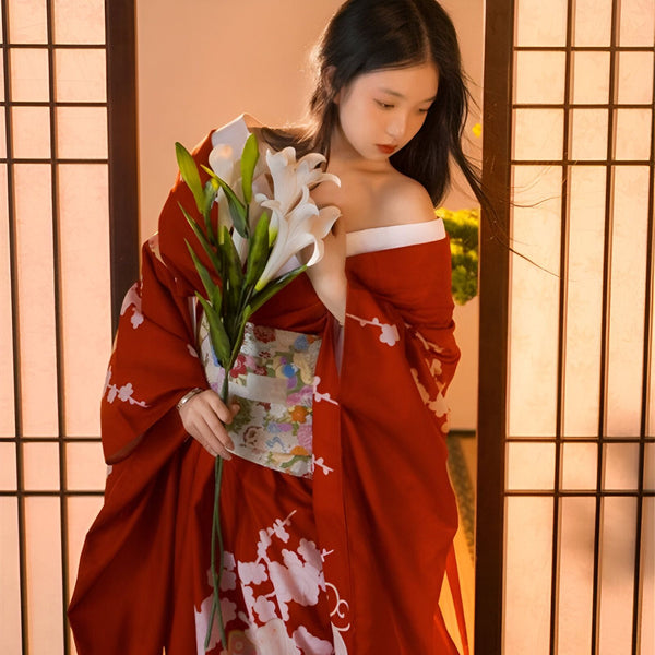 Femme asiatique portant un kimono rouge traditionnel avec des motifs floraux blancs. Elle tient un bouquet de lys blancs. Vente de kimonos en ligne.