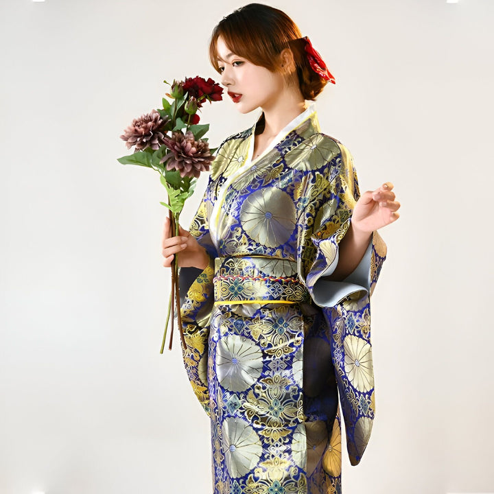 Femme en kimono traditionnel bleu et doré avec des motifs floraux, tenant un bouquet de fleurs. Vente de kimonos authentiques.