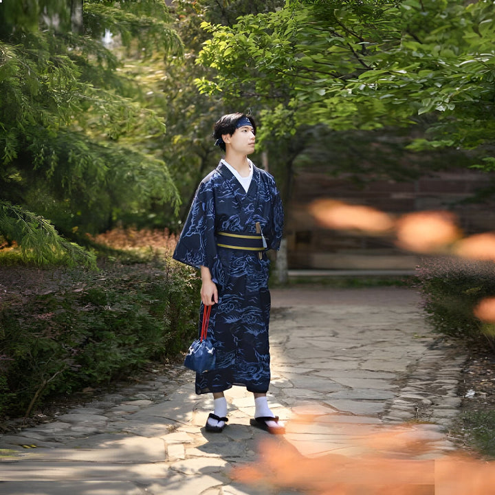 Homme portant un kimono japonais bleu marine avec motifs, ceinture obi dorée, tenant un petit sac. Vente de kimonos traditionnels et modernes en ligne. Découvrez notre collection.