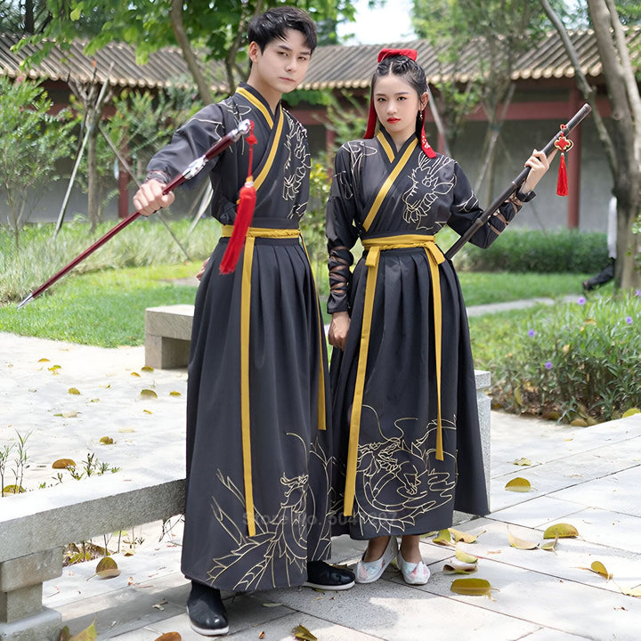 Couple en kimonos traditionnels chinois noirs avec motifs dorés et ceintures jaunes. Ils tiennent des armes décoratives. Vêtements authentiques pour arts martiaux ou événements culturels. Découvrez notre collection de kimonos.