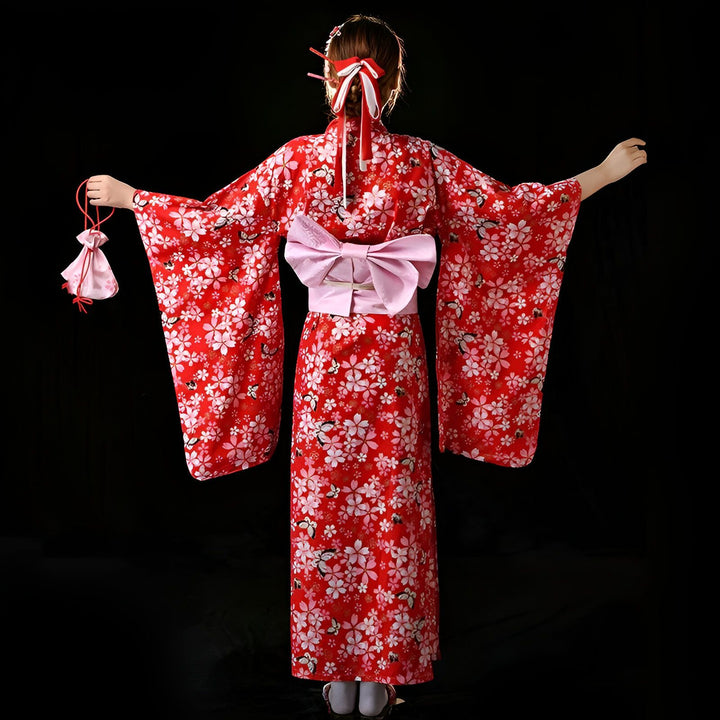 Vue arrière d'une femme portant un kimono rouge à motifs de fleurs blanches. Un obi rose est noué à la taille. Elle tient un petit sac rose dans sa main droite.