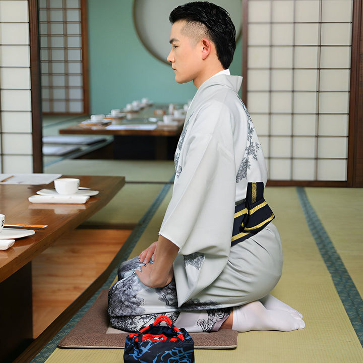 Homme en kimono gris clair assis au sol dans un intérieur japonais traditionnel. Vente de kimonos authentiques.