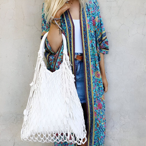 Femme portant un kimono fleuri bleu et un sac à main en macramé blanc. Vêtements de style bohème en vente. Collection de kimonos uniques et élégants.