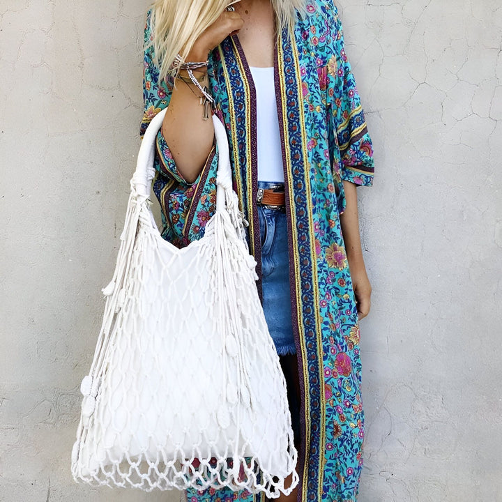 Femme portant un kimono fleuri bleu et un sac à main en macramé blanc. Vêtements de style bohème en vente. Collection de kimonos uniques et élégants.