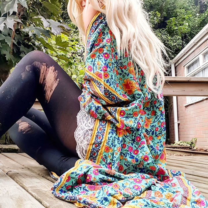 Femme blonde assise portant un kimono fleuri coloré avec des motifs orientaux et des collants noirs déchirés. Kimonos pour femmes. Mode bohème chic.