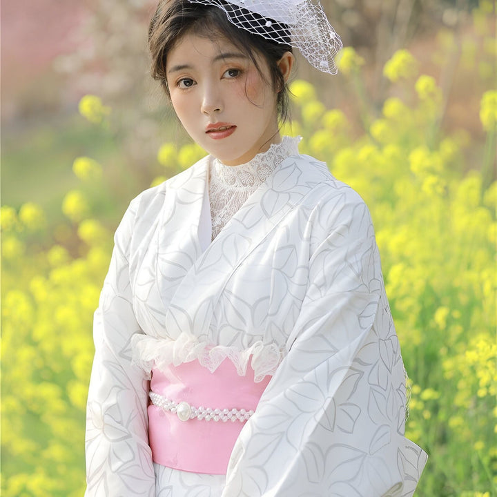 Femme en kimono blanc à motifs floraux avec ceinture rose. Disponible dans notre boutique en ligne.