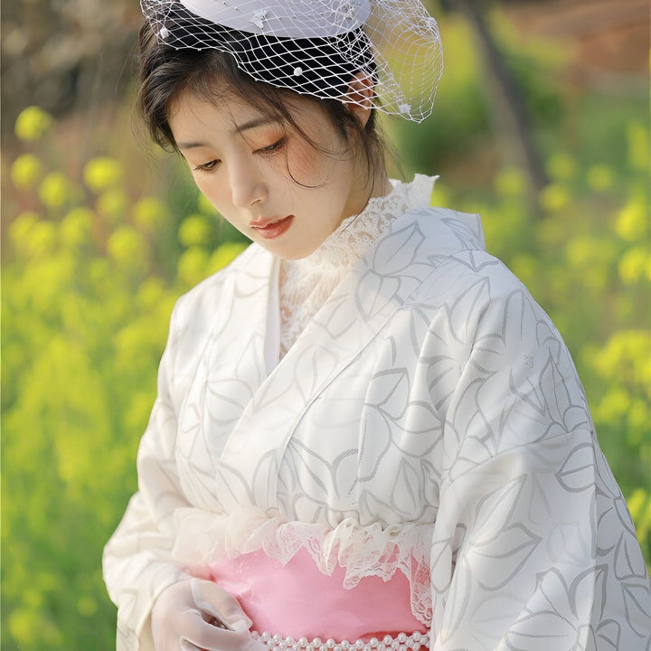 Femme portant un kimono blanc à motifs floraux avec ceinture rose et chapeau orné de voile. Kimonos élégants à vendre.