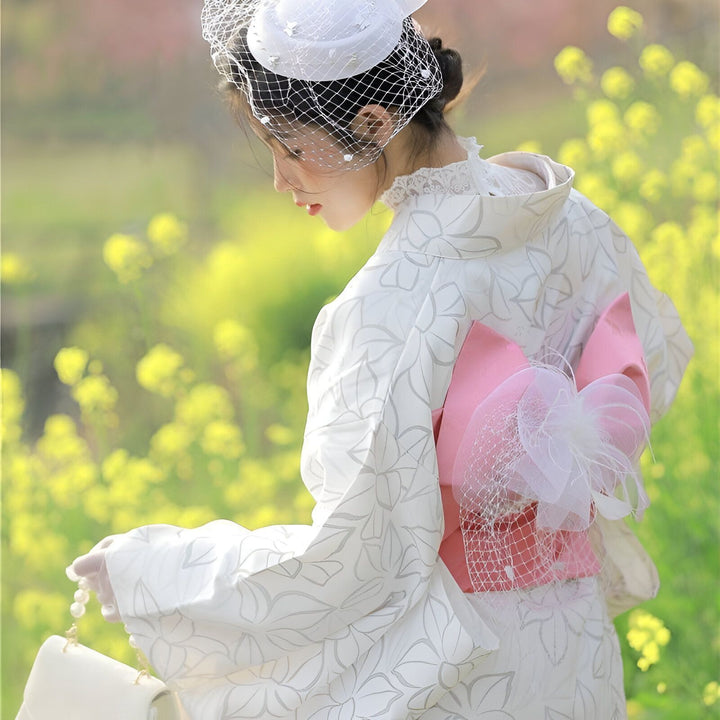Femme portant un kimono blanc à motifs floraux avec une ceinture rose, chapeau blanc à voilette. Kimonos traditionnels japonais en vente.