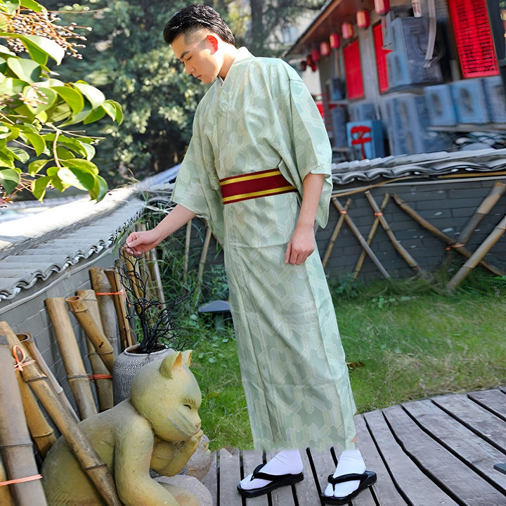 Homme portant un kimono japonais vert clair avec une ceinture obi rouge et or. Sandales traditionnelles geta. Vente de kimonos authentiques en ligne.