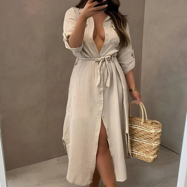 Femme portant une robe kimono beige boutonnée, nouée à la taille, avec une fente. Elle prend un selfie dans un miroir et tient un sac en paille. Kimonos élégants et confortables pour toutes les occasions.