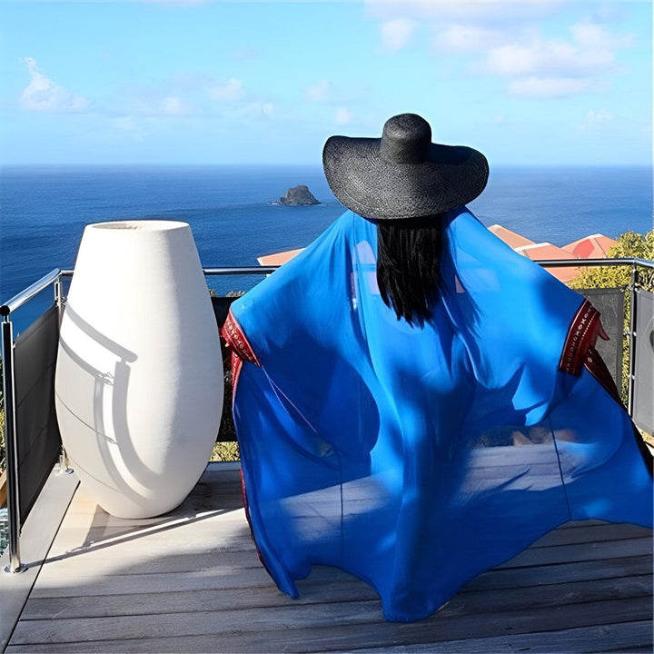 Femme portant un kimono bleu et un grand chapeau noir, regardant l'océan depuis une terrasse. Vente de kimonos en ligne.