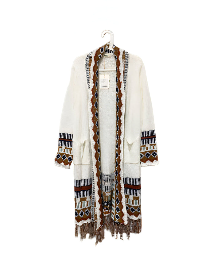 Kimono long blanc à motifs géométriques et franges, suspendu sur un cintre. Vêtement d'extérieur tendance pour femmes, idéal pour ajouter une touche bohème à votre garde-robe. Achetez nos kimonos uniques en ligne.