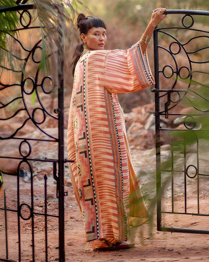 Femme portant un kimono à rayures orange et motifs, posant devant un portail en fer forgé. Kimonos à la vente sur notre site.