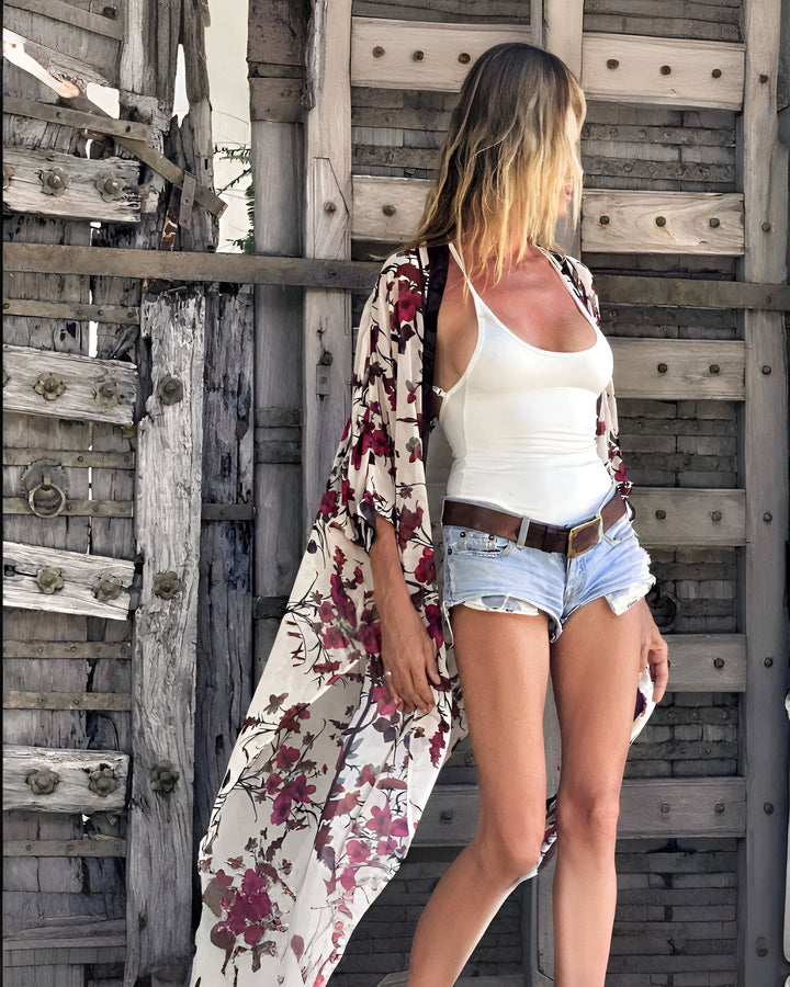 Femme portant un kimono fleuri devant une porte en bois rustique. Découvrez notre collection de kimonos pour un look élégant et décontracté.