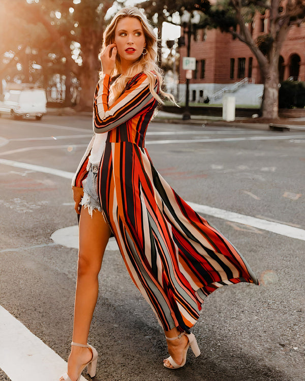 Femme blonde portant un kimono rayé coloré, un short en jean et des talons hauts. Kimono tendance pour une allure élégante et décontractée. Collection de kimonos chics.