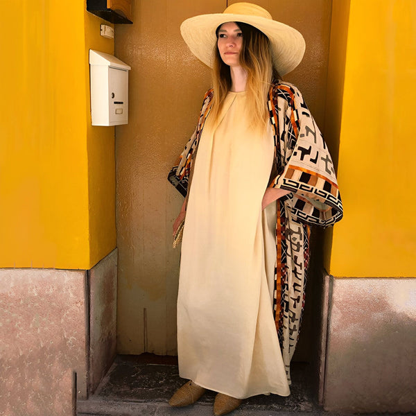 Femme portant un kimono à motifs devant un mur jaune. Chapeau de paille et robe beige. Kimonos à la mode pour toutes les occasions.