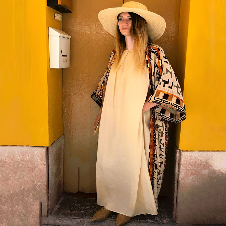 Femme portant un kimono à motifs devant un mur jaune. Chapeau de paille et robe beige. Kimonos à la mode pour toutes les occasions.