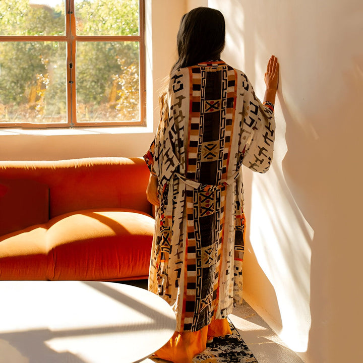 Femme portant un kimono long imprimé dans un intérieur ensoleillé. Vente de kimonos pour femmes, styles variés et confortables.