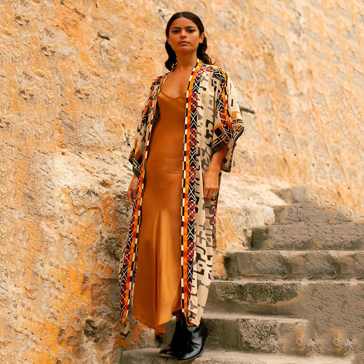 Femme portant un kimono à motifs ethniques et une robe en soie couleur or. Kimono parfait pour un look bohème chic.