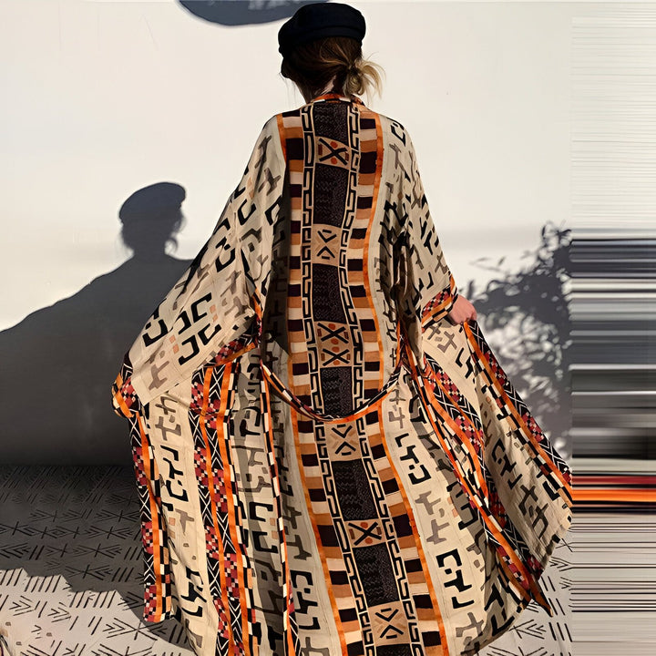 Femme portant un kimono long à motifs ethniques. Kimono beige, noir et orange, disponible à l'achat. Vêtements de style japonais revisités.