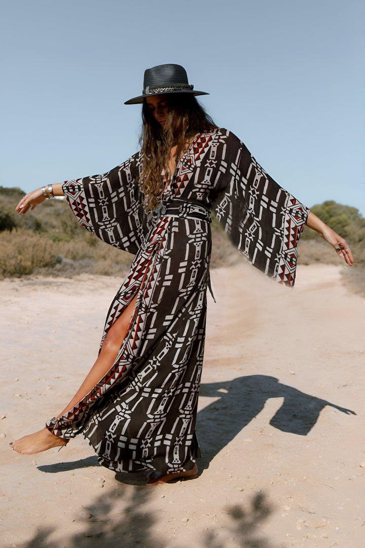 Femme portant un kimono long à motifs boho sur un chemin de terre. Chapeau noir, fente sur la jambe, manches amples. Vêtements kimono pour femmes, style bohème.