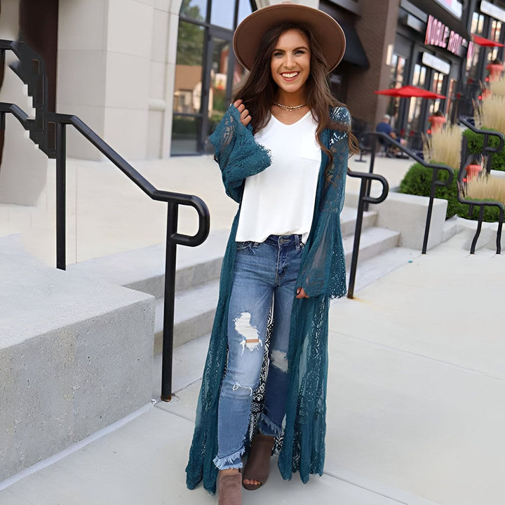 Femme souriante portant un kimono en dentelle turquoise, un jean déchiré et un chapeau marron. Vente de kimonos en ligne.