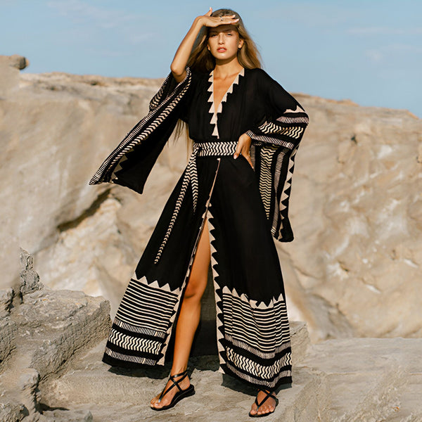 Femme portant un kimono noir à motifs géométriques blancs. Kimono long, ample avec ceinture. Vêtement de plage tendance et élégant.