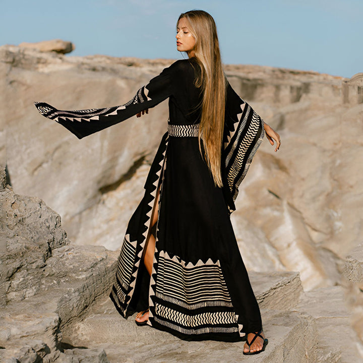 Femme blonde portant un kimono noir long à motifs clairs, manches amples. Vêtement de plage chic et décontracté. Notre collection de kimonos.