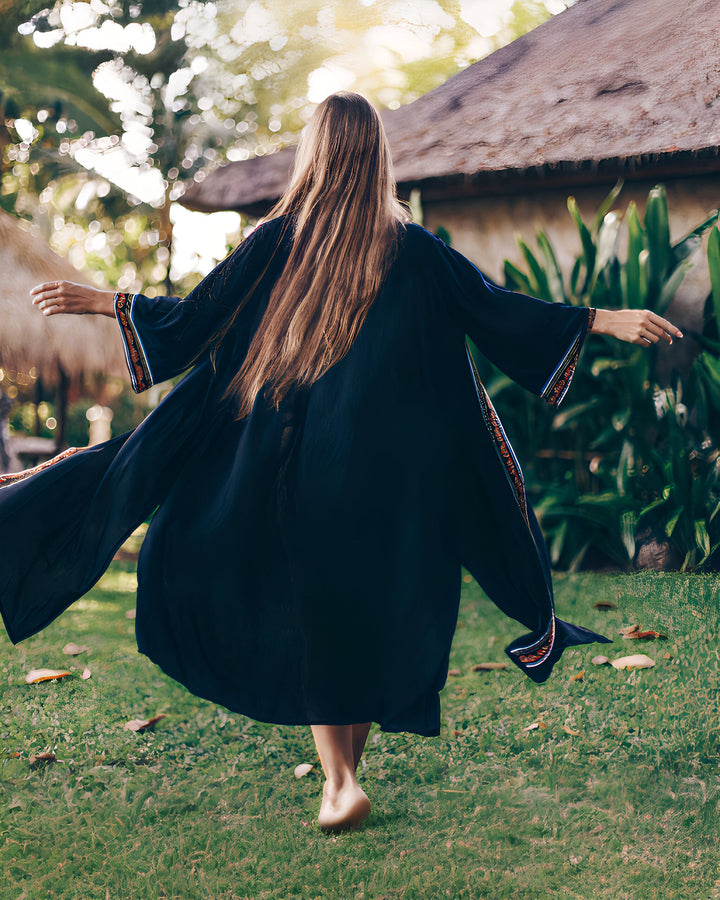 Femme portant un kimono noir, vue de dos, marchant pieds nus dans l'herbe. Kimonos de qualité disponibles dans notre boutique en ligne.