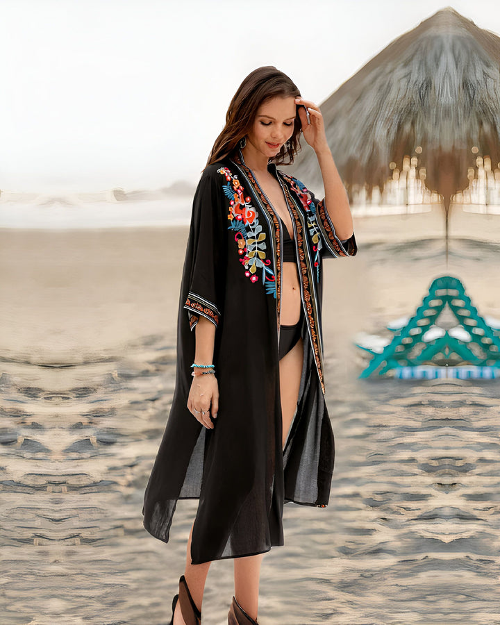 Femme portant un kimono noir brodé sur une plage. Kimono élégant, parfait comme vêtement de plage ou pour ajouter une touche bohème à votre garde-robe. Découvrez notre collection de kimonos.