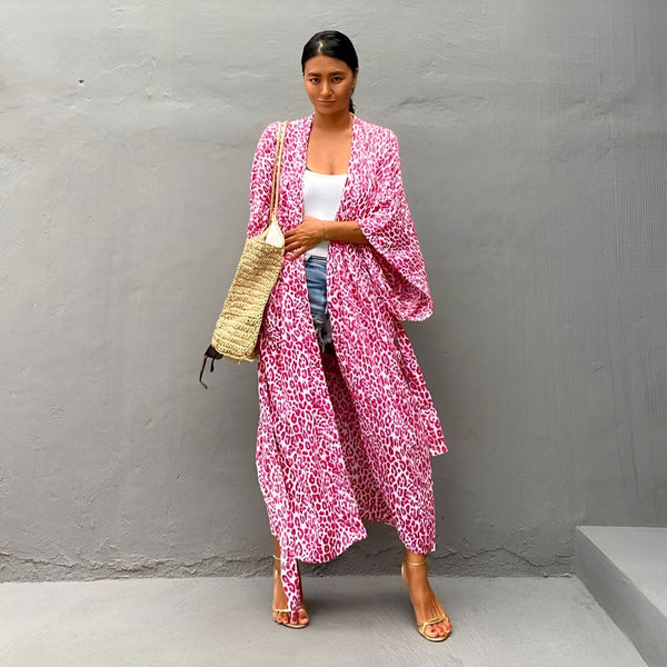 Femme portant un kimono rose à motifs léopard, un débardeur blanc et un short en jean. Sac en paille sur l'épaule. Kimonos à la mode pour toutes les occasions.
