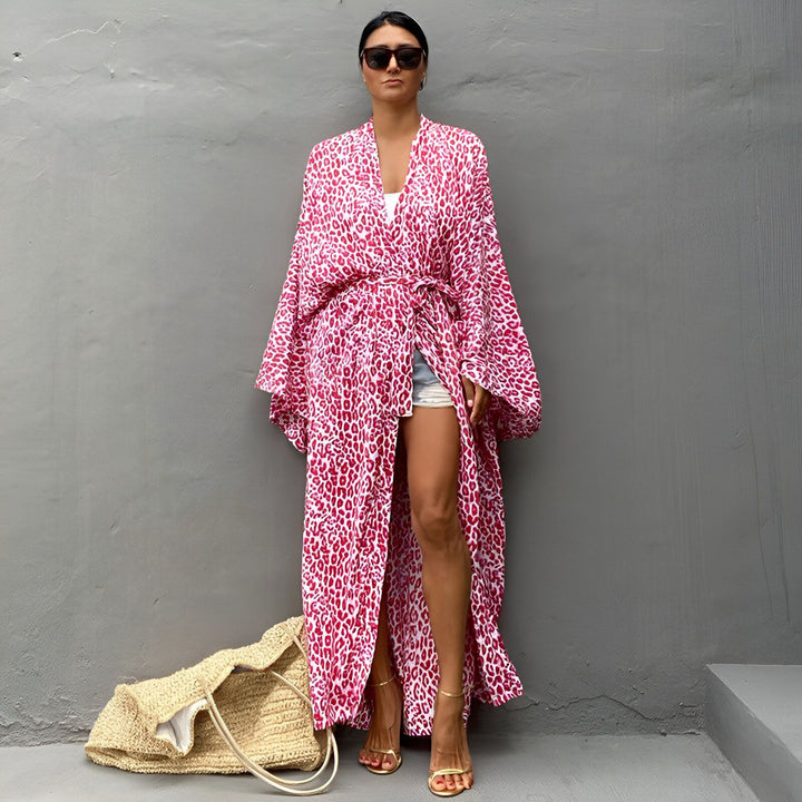 Femme portant un kimono long à motif léopard rose et blanc. Vente de kimonos pour femmes. Kimono de plage tendance. Sac en paille. Lunettes de soleil stylées.