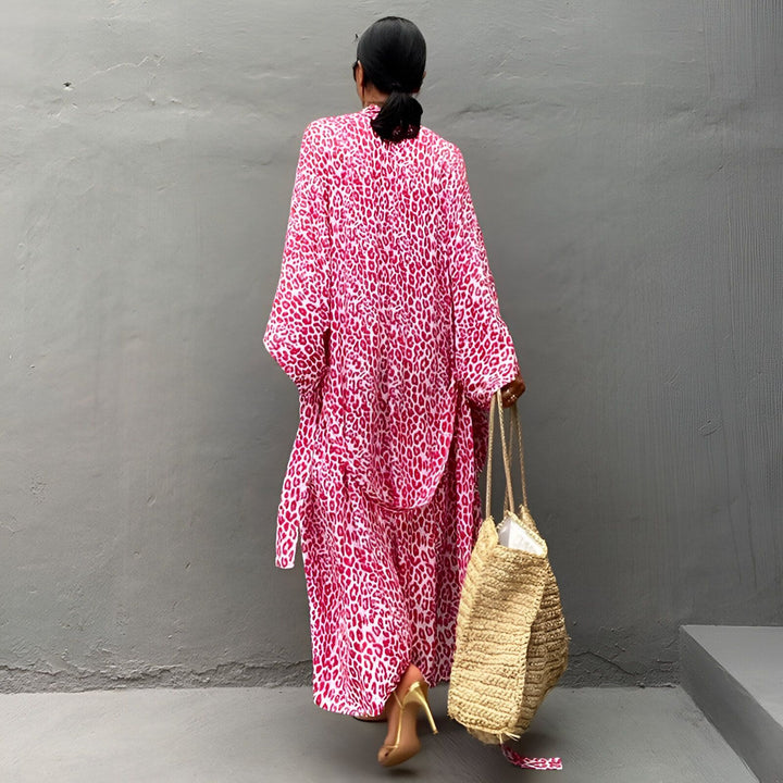 Femme portant un kimono long rose imprimé léopard, vue de dos. Elle tient un sac en paille et porte des chaussures dorées à talons. Kimonos tendance pour femmes.