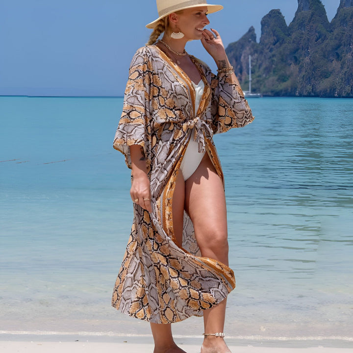 Femme souriante portant un kimono motif serpent sur la plage tropicale. Vêtements de plage, mode estivale. Découvrez notre collection de kimonos élégants.