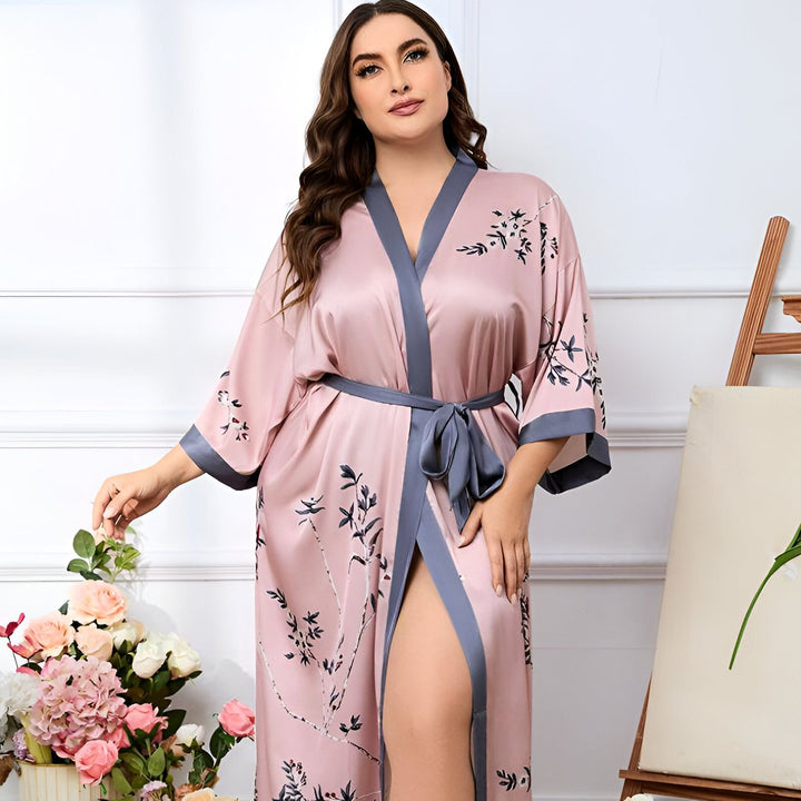 Femme portant un kimono rose en satin avec motifs floraux. Peignoir élégant pour la maison, vêtement d'intérieur confortable et raffiné. Disponible dans notre boutique de kimonos.