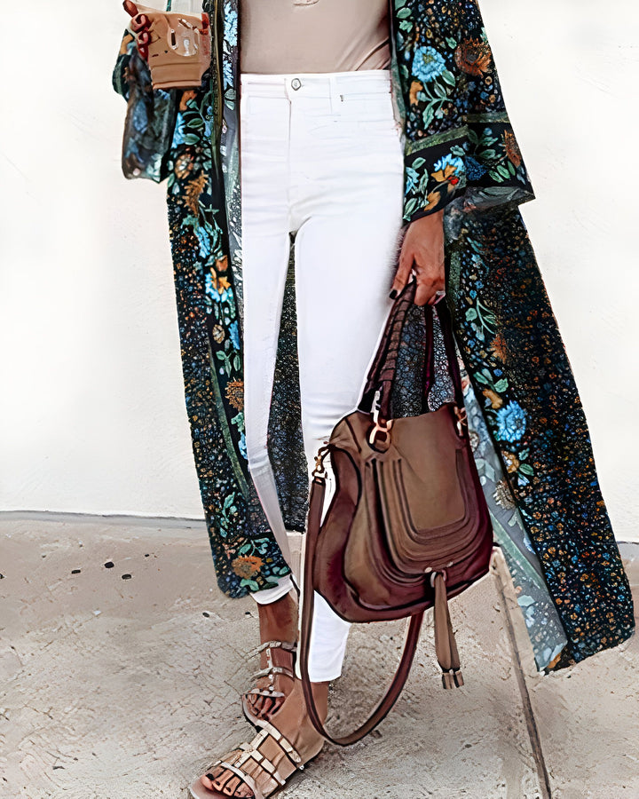 Kimono long fleuri porté par une femme en jean blanc, avec un sac en cuir marron et des sandales. Vêtements d'extérieur kimono fleuri disponible à l'achat. Mode kimono tendance.
