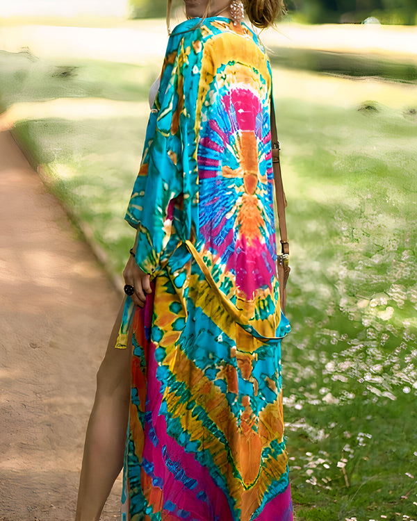 Femme portant un kimono long et coloré tie-dye, tons de bleu, jaune, rose. Vue arrière, elle marche dans un parc. Kimonos pour femmes, vêtements d'été, mode bohème.