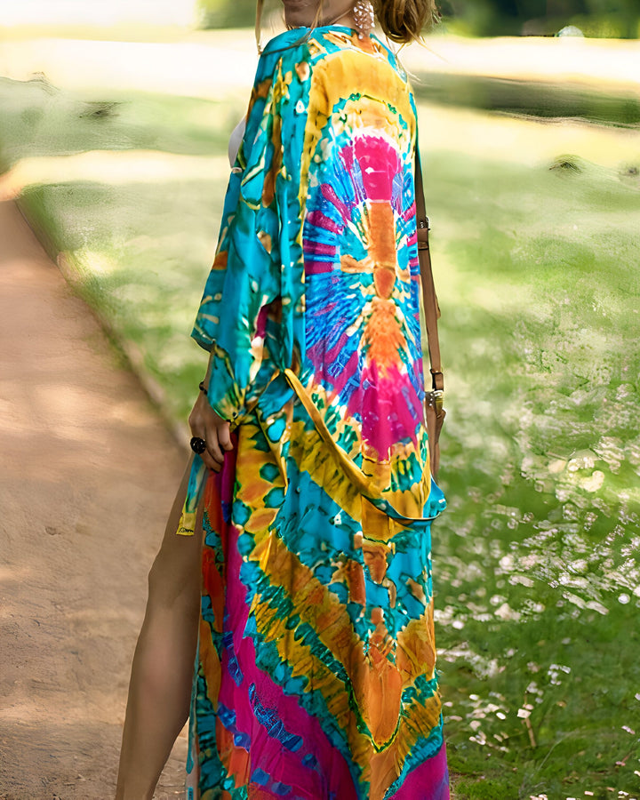 Femme portant un kimono long et coloré tie-dye, tons de bleu, jaune, rose. Vue arrière, elle marche dans un parc. Kimonos pour femmes, vêtements d'été, mode bohème.