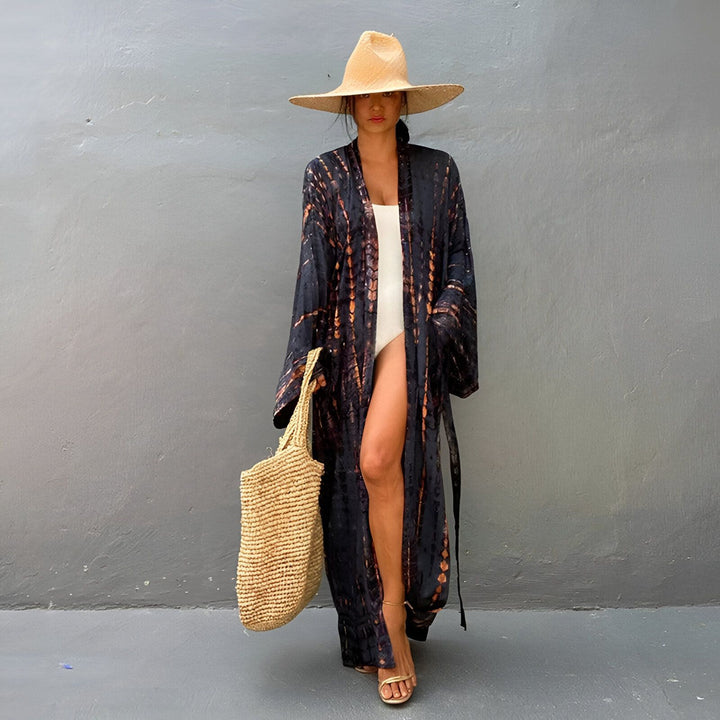 Femme portant un kimono long tie-dye noir et orange, un maillot de bain blanc, un chapeau de paille et un sac. Mode kimono d'été.