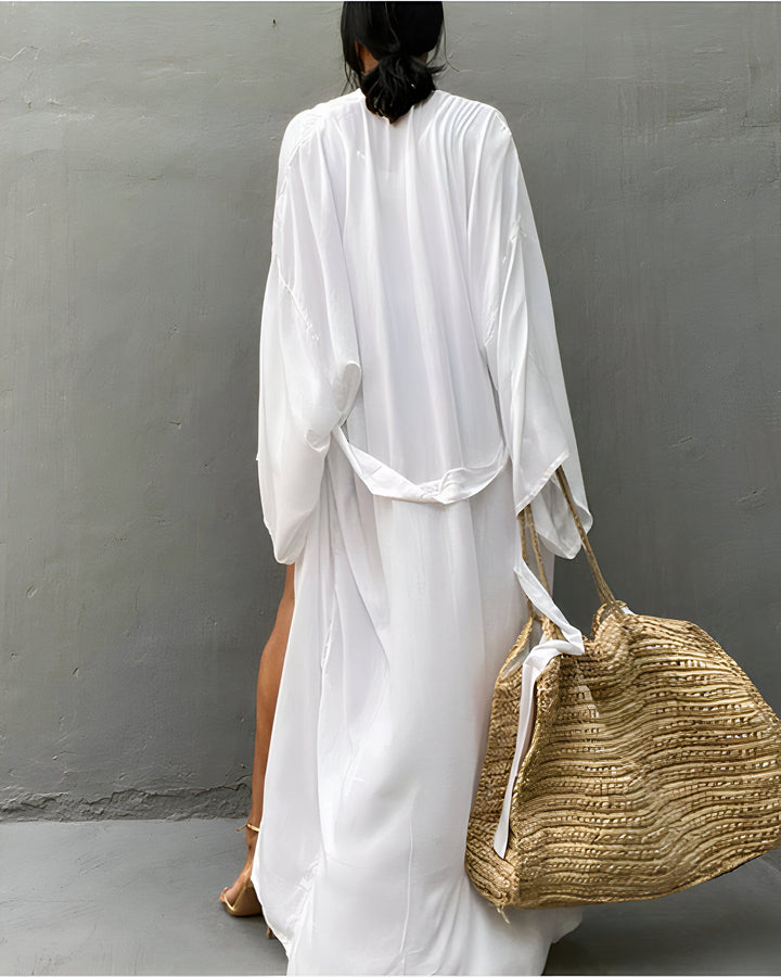 Femme vue de dos portant un kimono blanc long avec ceinture et un grand sac en paille. Vêtements de plage, vente de kimonos en ligne.