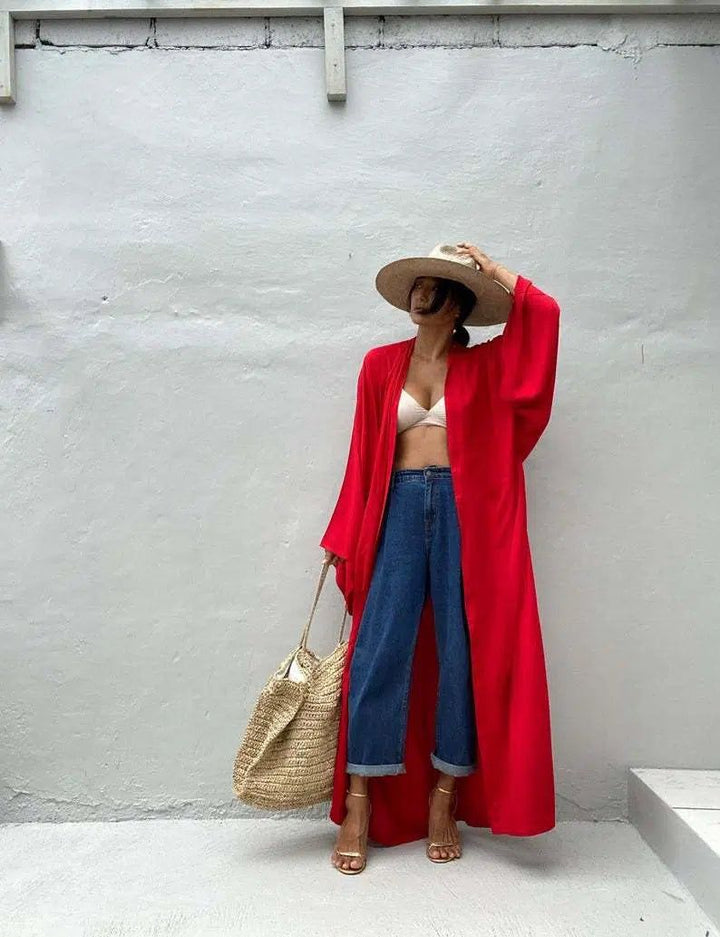 Femme portant un kimono rouge vibrant, jean taille haute, chapeau de paille, et sac. Élégance décontractée. Découvrez notre collection de kimonos uniques pour un style tendance et confortable.