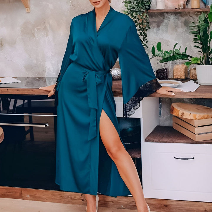 Femme portant un kimono bleu en soie avec des manches évasées et des détails en dentelle noire. Peignoir élégant avec ceinture. Vêtements de détente de luxe pour femme. Idéal pour se sentir belle à la maison.