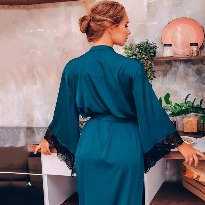 Femme portant un kimono bleu sarcelle avec des détails en dentelle noire, vue de dos. Élégant peignoir de notre collection de kimonos.