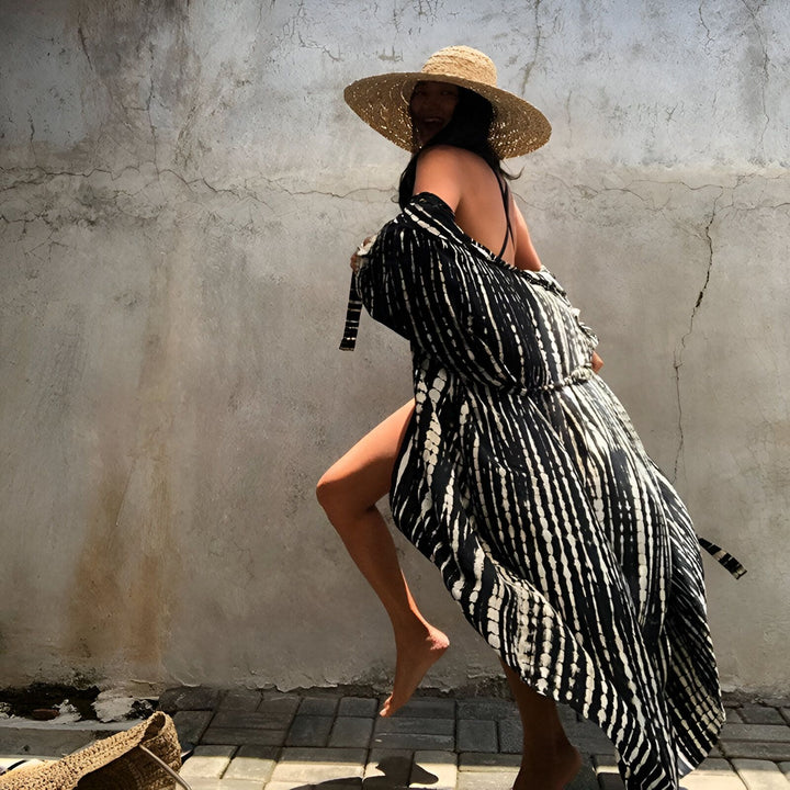 Femme souriante portant un kimono rayé noir et blanc, chapeau de paille. Look estival et décontracté. Découvrez notre collection de kimonos tendance.