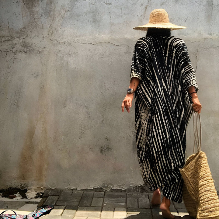 Femme portant un kimono rayé noir et blanc avec un chapeau de paille. Sac en osier à l'épaule. Collection de kimonos tendances.