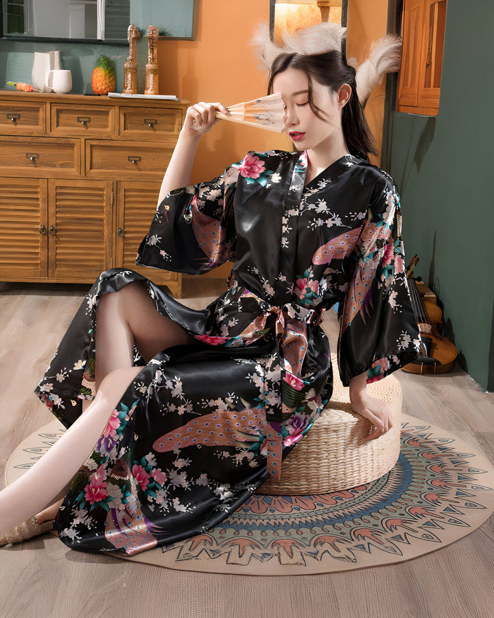 Femme en kimono noir à motifs floraux et paons, assise avec un éventail. Kimono en soie, vêtement japonais traditionnel. Collection de kimonos élégants.