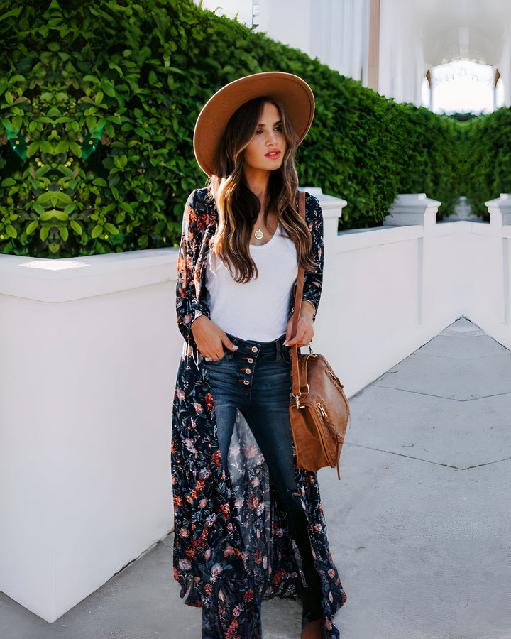 Femme portant un kimono long à motifs floraux, avec un chapeau marron et un jean. Style décontracté et élégant. Découvrez notre collection de kimonos uniques.