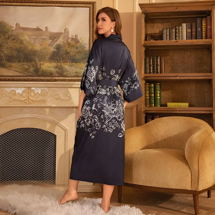 Femme portant un kimono bleu marine à motifs floraux devant une cheminée et une bibliothèque. Découvrez notre collection de kimonos élégants.
