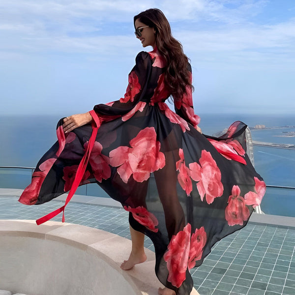 Femme portant un kimono long et fluide à motifs floraux rouges et noirs. Kimono de notre collection, idéal pour un style élégant et décontracté. Vue sur mer en arrière-plan.